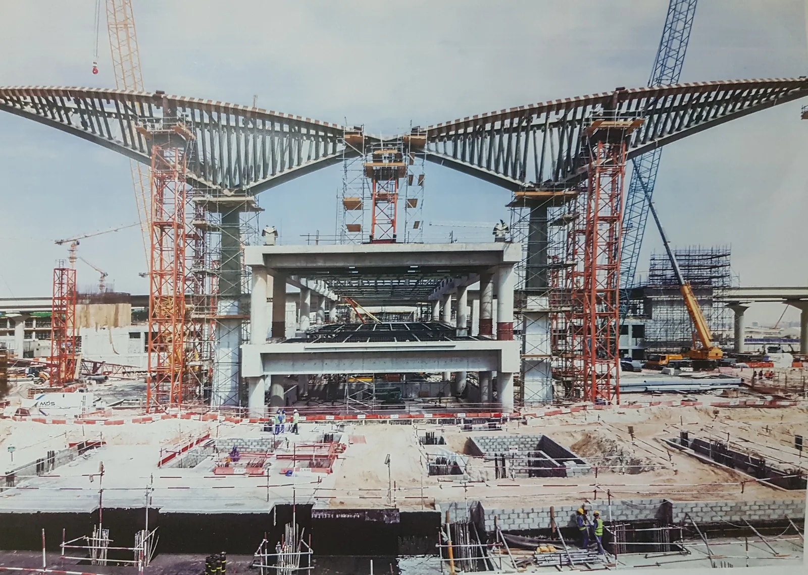 A Route 2020 metro station under construction, its canopy trusses raised over the platform
